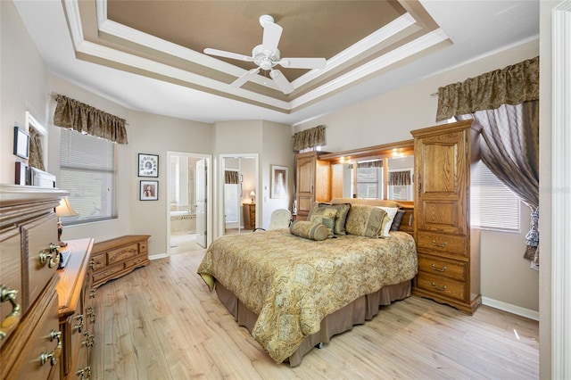 bedroom with light wood-style flooring, a raised ceiling, and ensuite bath