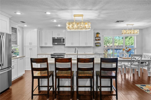kitchen with dark wood-style flooring, appliances with stainless steel finishes, light countertops, a textured ceiling, and visible vents