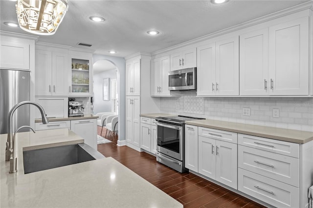 kitchen with appliances with stainless steel finishes, arched walkways, a sink, white cabinets, and dark wood-style floors