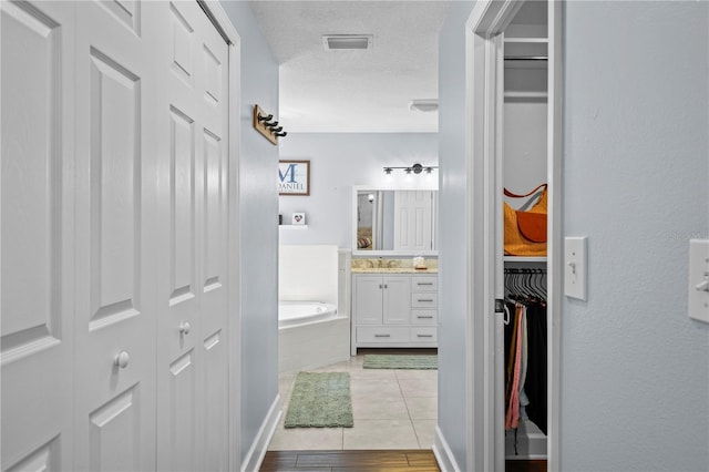 full bathroom featuring a garden tub, a textured ceiling, visible vents, vanity, and a spacious closet