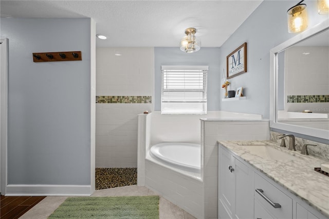 full bathroom featuring a textured ceiling, walk in shower, a bath, and vanity
