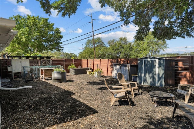 view of yard with a storage shed, a vegetable garden, a fenced backyard, an outbuilding, and a fire pit
