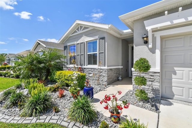 view of exterior entry with an attached garage, stucco siding, and stone siding