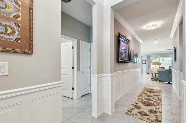 hallway featuring crown molding, a decorative wall, and wainscoting