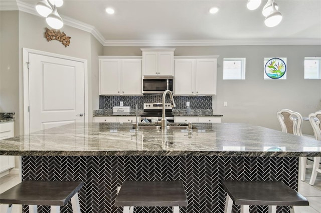 kitchen with a breakfast bar, stainless steel appliances, white cabinetry, tasteful backsplash, and a center island with sink