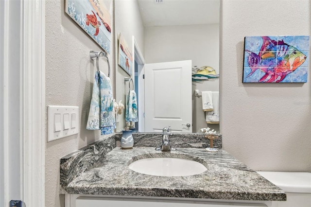 half bathroom with vanity, a textured wall, and toilet