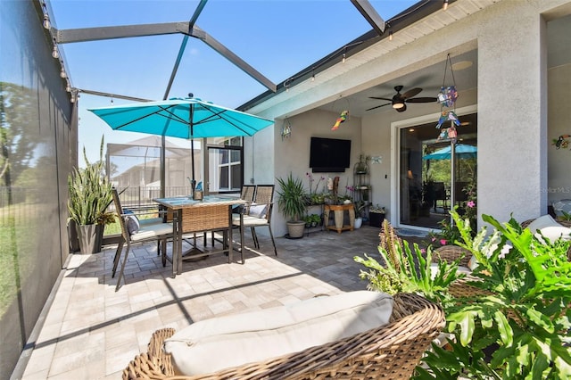 view of patio featuring outdoor dining space, ceiling fan, and glass enclosure