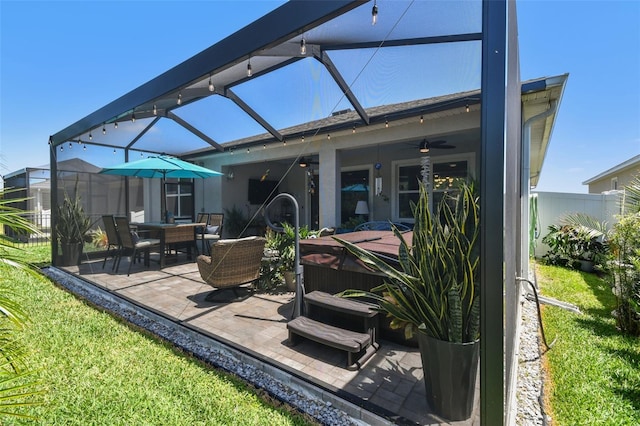 back of house with ceiling fan, a lawn, a hot tub, glass enclosure, and a patio