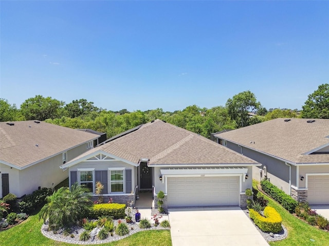 ranch-style house with a shingled roof, an attached garage, stone siding, stucco siding, and concrete driveway