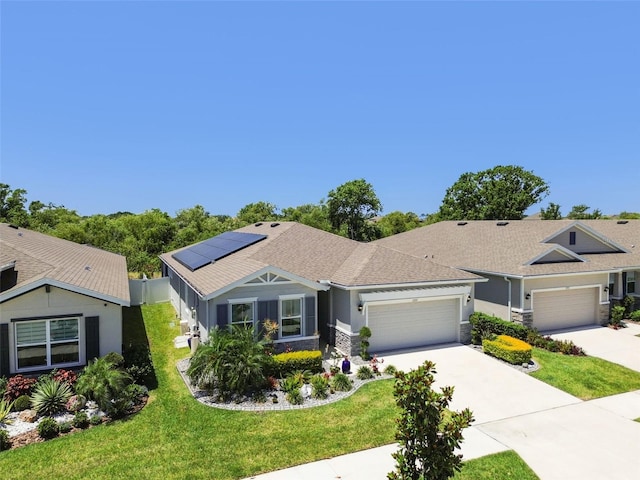 ranch-style home featuring a front yard, roof mounted solar panels, concrete driveway, an attached garage, and stone siding