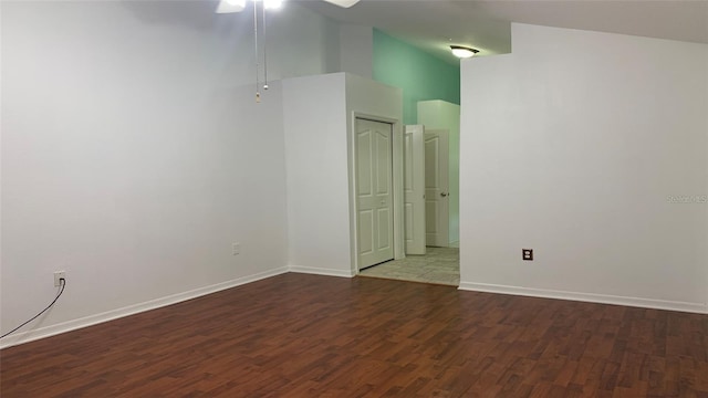 empty room featuring baseboards, ceiling fan, wood finished floors, and a towering ceiling