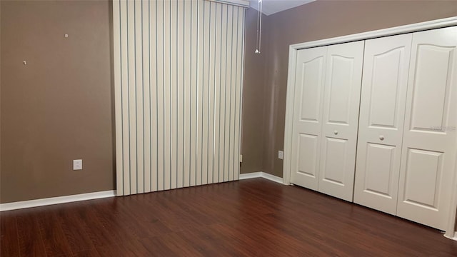 unfurnished bedroom with baseboards, dark wood finished floors, and a closet