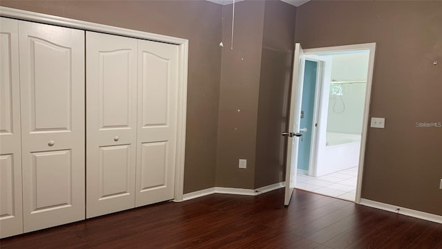 unfurnished bedroom featuring baseboards, dark wood-style flooring, and a closet