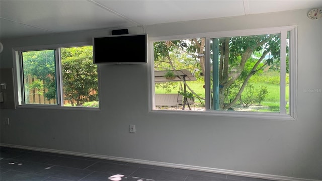 spare room with baseboards, a wealth of natural light, and dark tile patterned flooring