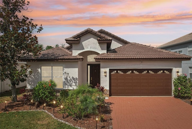 mediterranean / spanish-style home with a garage, stucco siding, driveway, and a tile roof