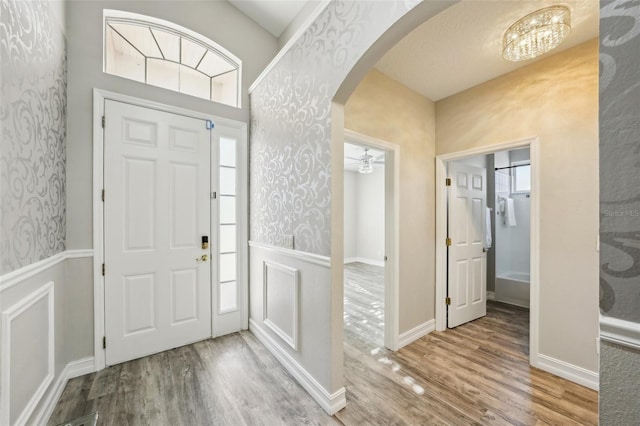 foyer featuring arched walkways, a wainscoted wall, wallpapered walls, and wood finished floors