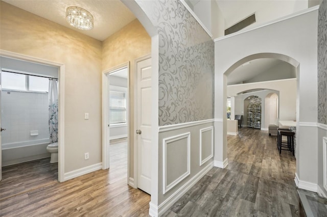 hallway featuring baseboards, arched walkways, and wood finished floors