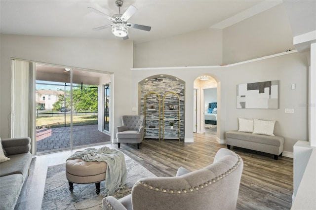 living room with wood finished floors, baseboards, ceiling fan, high vaulted ceiling, and arched walkways