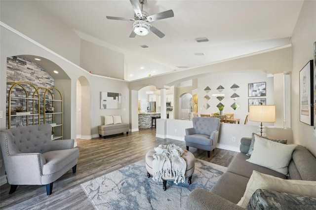 living area featuring wood finished floors, arched walkways, decorative columns, and lofted ceiling