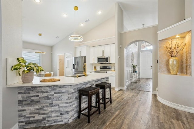 kitchen with wood finished floors, a kitchen breakfast bar, white cabinets, decorative light fixtures, and stainless steel appliances