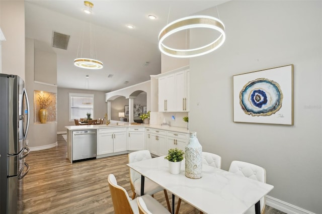 kitchen with arched walkways, appliances with stainless steel finishes, white cabinetry, and light wood-style flooring
