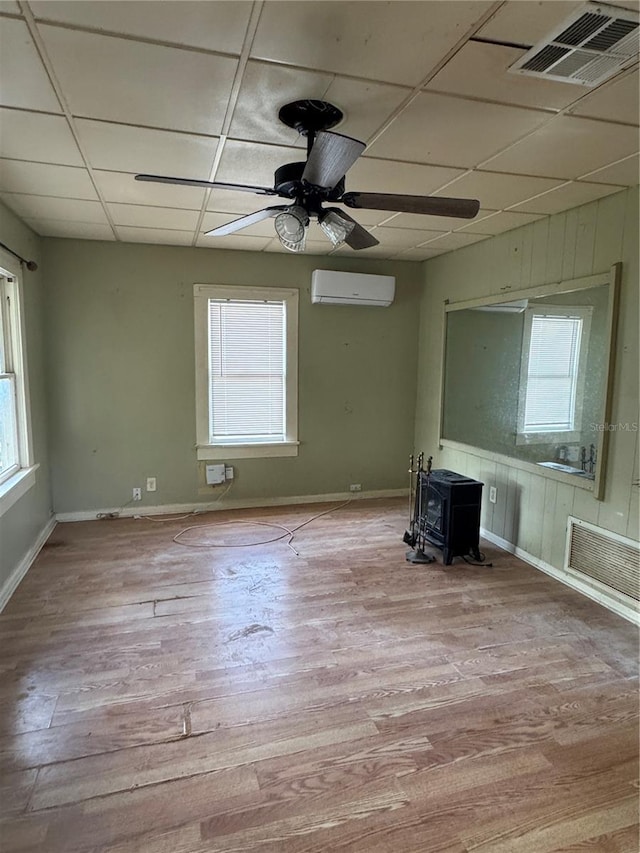 unfurnished living room featuring a healthy amount of sunlight, a wood stove, wood finished floors, and visible vents