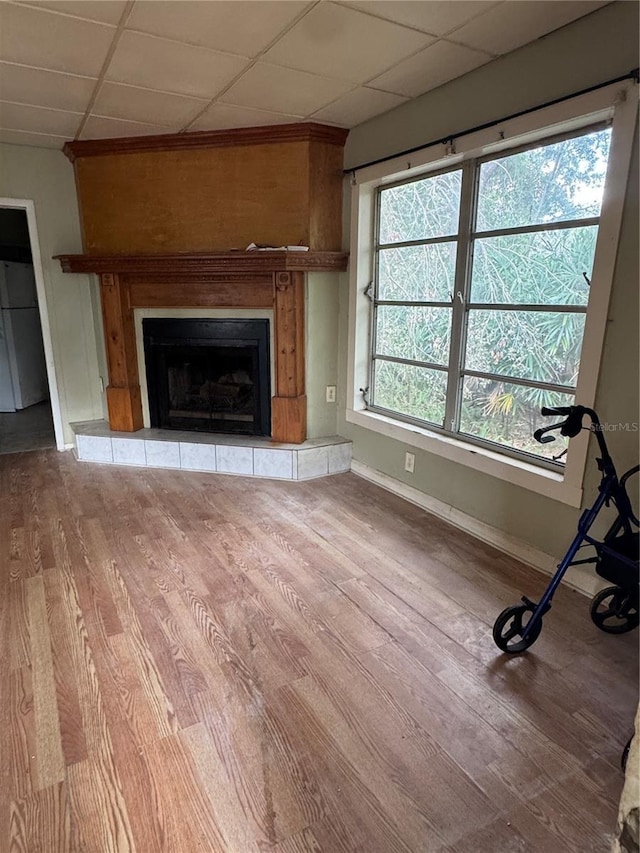 unfurnished living room with a tiled fireplace, baseboards, and wood finished floors