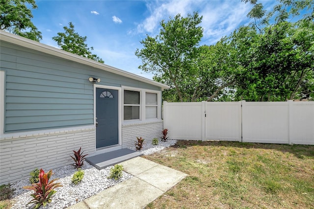 6601 13th St N, Saint Petersburg, FL 33702 - doorway to property featuring fence, a yard, and brick siding