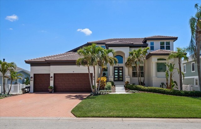 mediterranean / spanish-style home with stucco siding, an attached garage, a tile roof, and a front yard