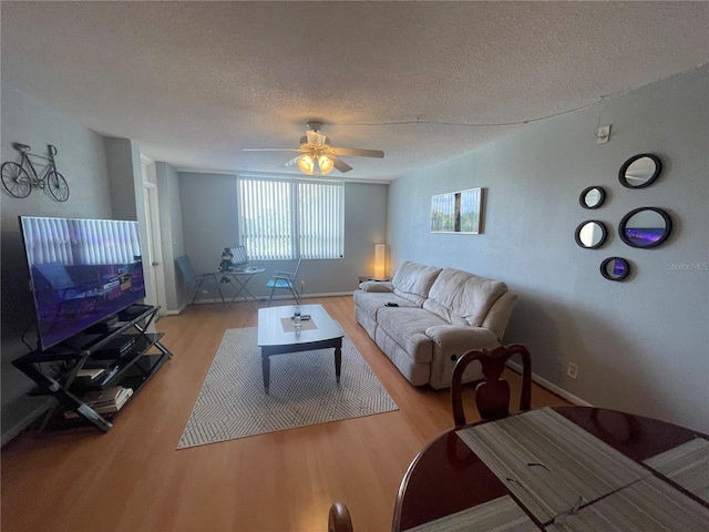 living room featuring baseboards, light wood-style flooring, a textured ceiling, and a ceiling fan