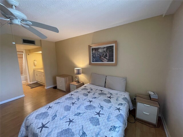 bedroom with baseboards, visible vents, wood finished floors, and ensuite bath