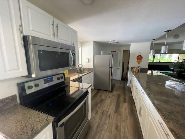 kitchen with appliances with stainless steel finishes, a sink, dark stone countertops, white cabinetry, and dark wood-type flooring