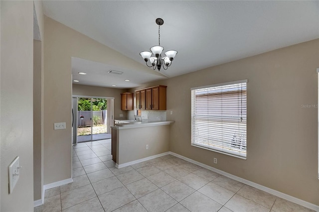 kitchen with a notable chandelier, light countertops, brown cabinetry, light tile patterned floors, and lofted ceiling
