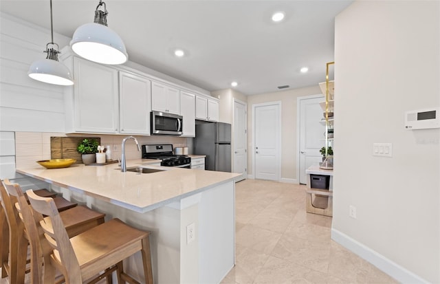 kitchen with a sink, stainless steel appliances, a peninsula, white cabinetry, and a kitchen bar