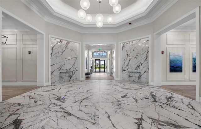foyer featuring crown molding, a raised ceiling, marble finish floor, and a chandelier