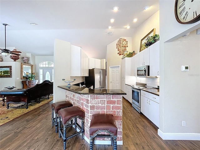 5058 Westlake Blvd, Dade City, FL 33523 - kitchen featuring appliances with stainless steel finishes, dark countertops, a peninsula, dark wood-style floors, and white cabinetry