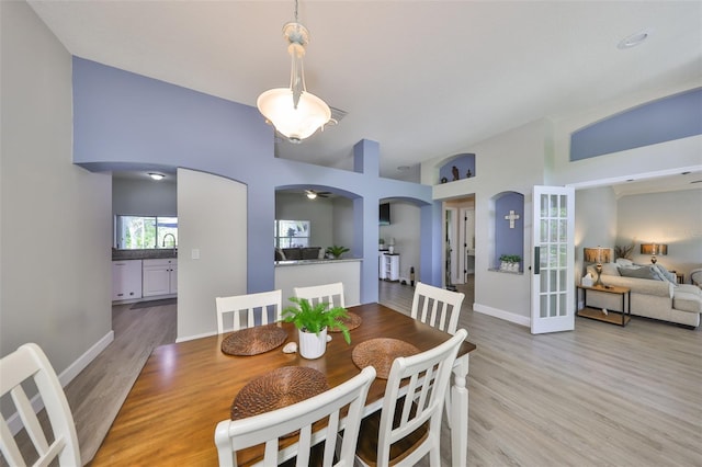 dining space featuring ceiling fan, visible vents, arched walkways, light wood-type flooring, and baseboards