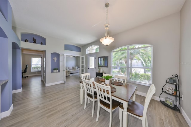 dining room featuring arched walkways, baseboards, and light wood finished floors