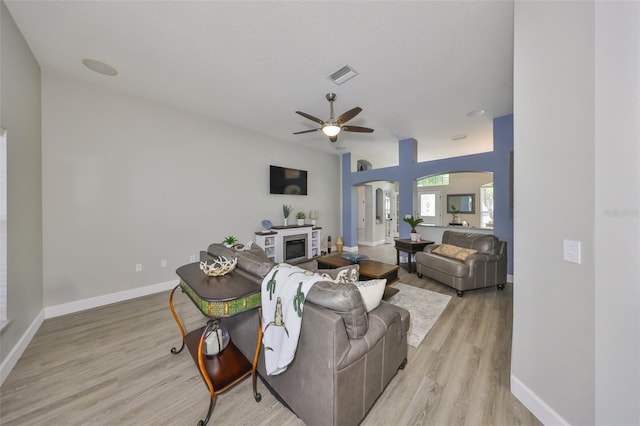 living room featuring ceiling fan, visible vents, arched walkways, baseboards, and light wood-style flooring