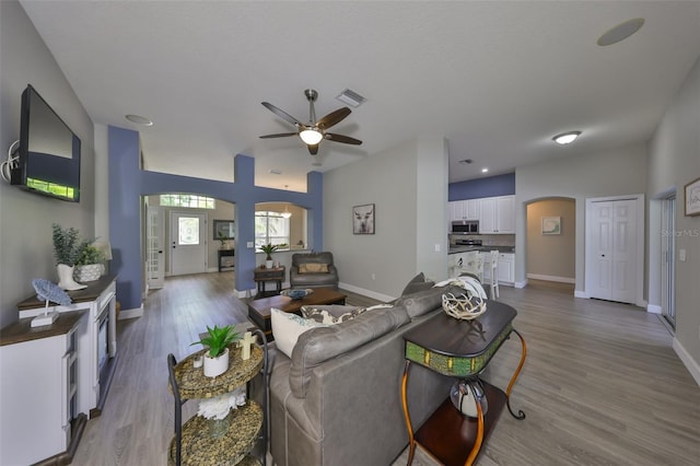 living area with a ceiling fan, visible vents, arched walkways, wood finished floors, and baseboards