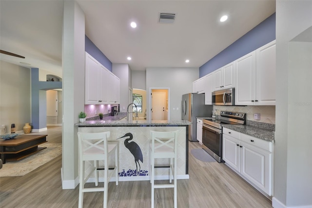 kitchen with light wood-style floors, a breakfast bar, stainless steel appliances, and visible vents