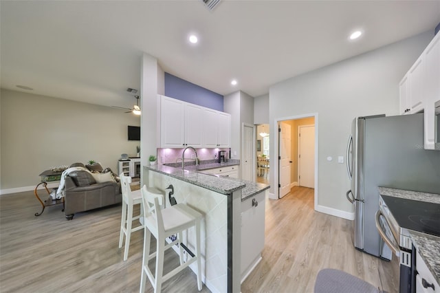 kitchen with stainless steel range with electric cooktop, light wood finished floors, white cabinetry, stone counters, and a kitchen bar