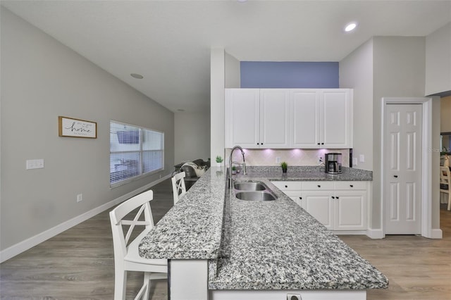 kitchen with light stone countertops, a sink, light wood finished floors, a peninsula, and white cabinetry