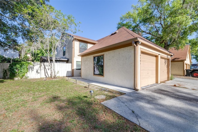 view of side of property with stucco siding, aphalt driveway, fence, and a yard