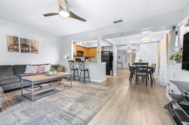 living area featuring ceiling fan, visible vents, baseboards, and light wood-type flooring