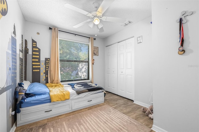 bedroom featuring a textured ceiling, a ceiling fan, wood finished floors, visible vents, and a closet