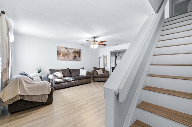 living area with ceiling fan, light wood finished floors, stairs, and a textured ceiling