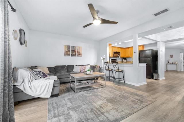 living area with visible vents, baseboards, ceiling fan, and light wood-type flooring