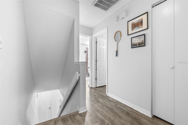 hall with baseboards, an upstairs landing, wood finished floors, and visible vents