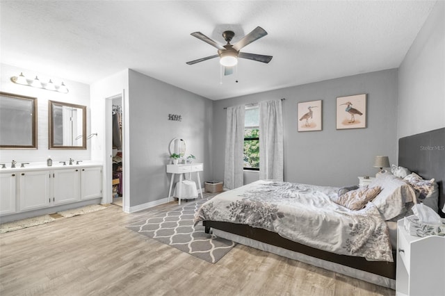 bedroom with light wood-style floors, baseboards, a walk in closet, ceiling fan, and connected bathroom